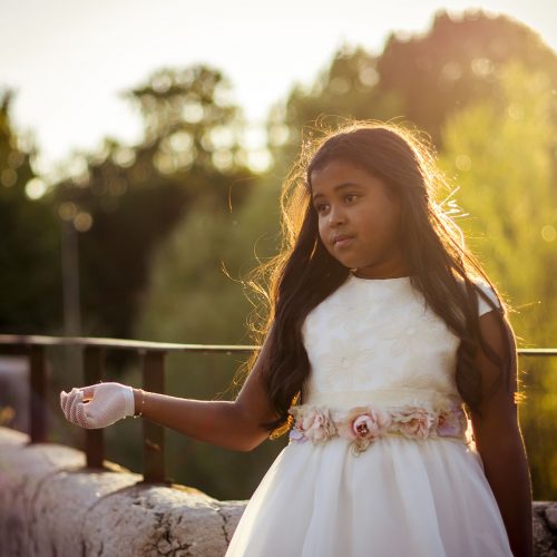 Fotografía de comunión de una niña vestida con un vestido blanco en un puente